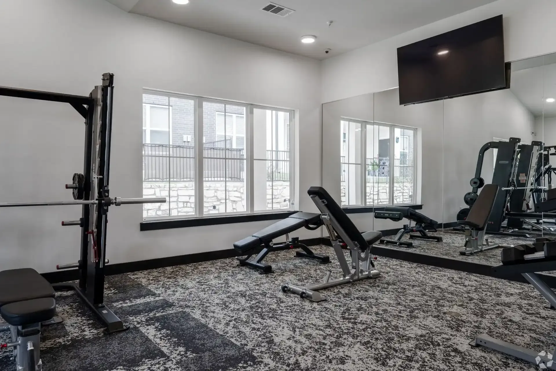 A gym with a lot of equipment, an oversized mirror, and a flat-screen TV on the wall at The Gabriel, which offers Leander, TX apartments for rent near Northtech Business Center.