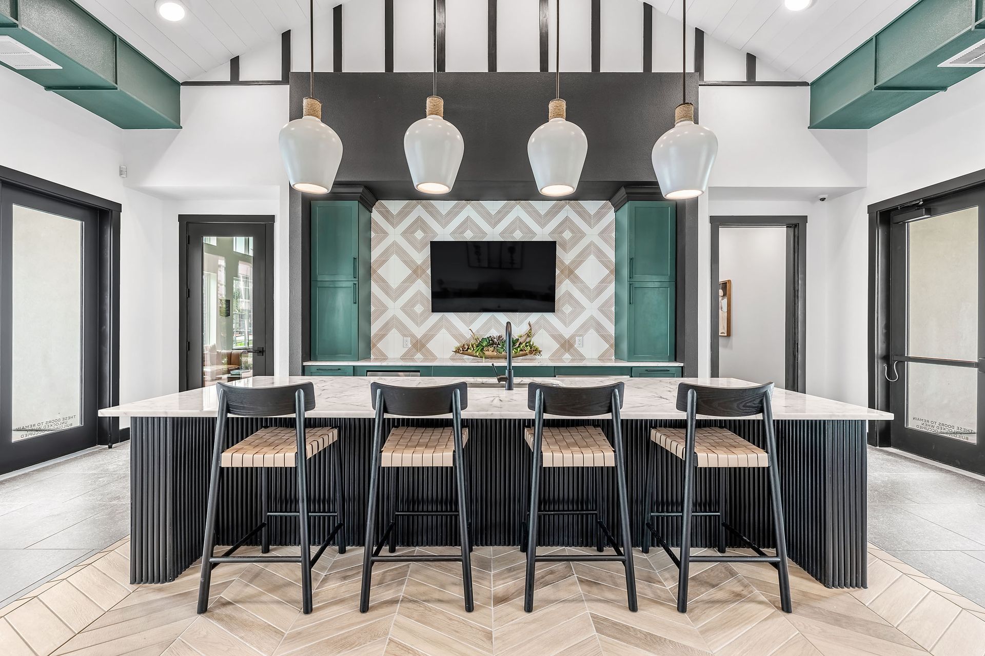 Clubhouse kitchen with a large island, stools, and a flat-screen TV at The Gabriel, which offers apartments for rent near Cedar Park.