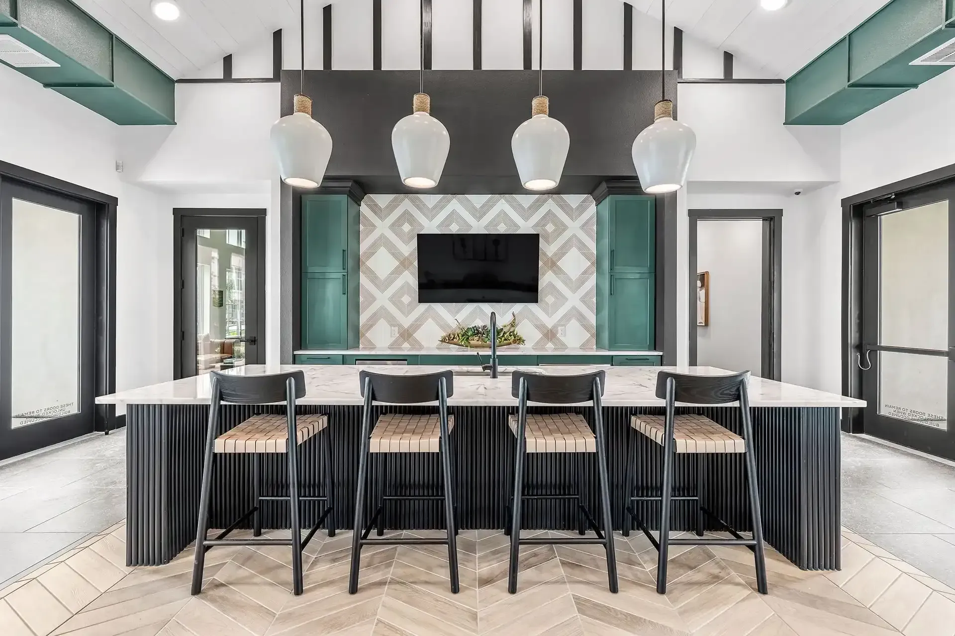 Clubhouse kitchen with a large island, stools, and a flat-screen TV at The Gabriel, which offers apartments for rent near Cedar Park.