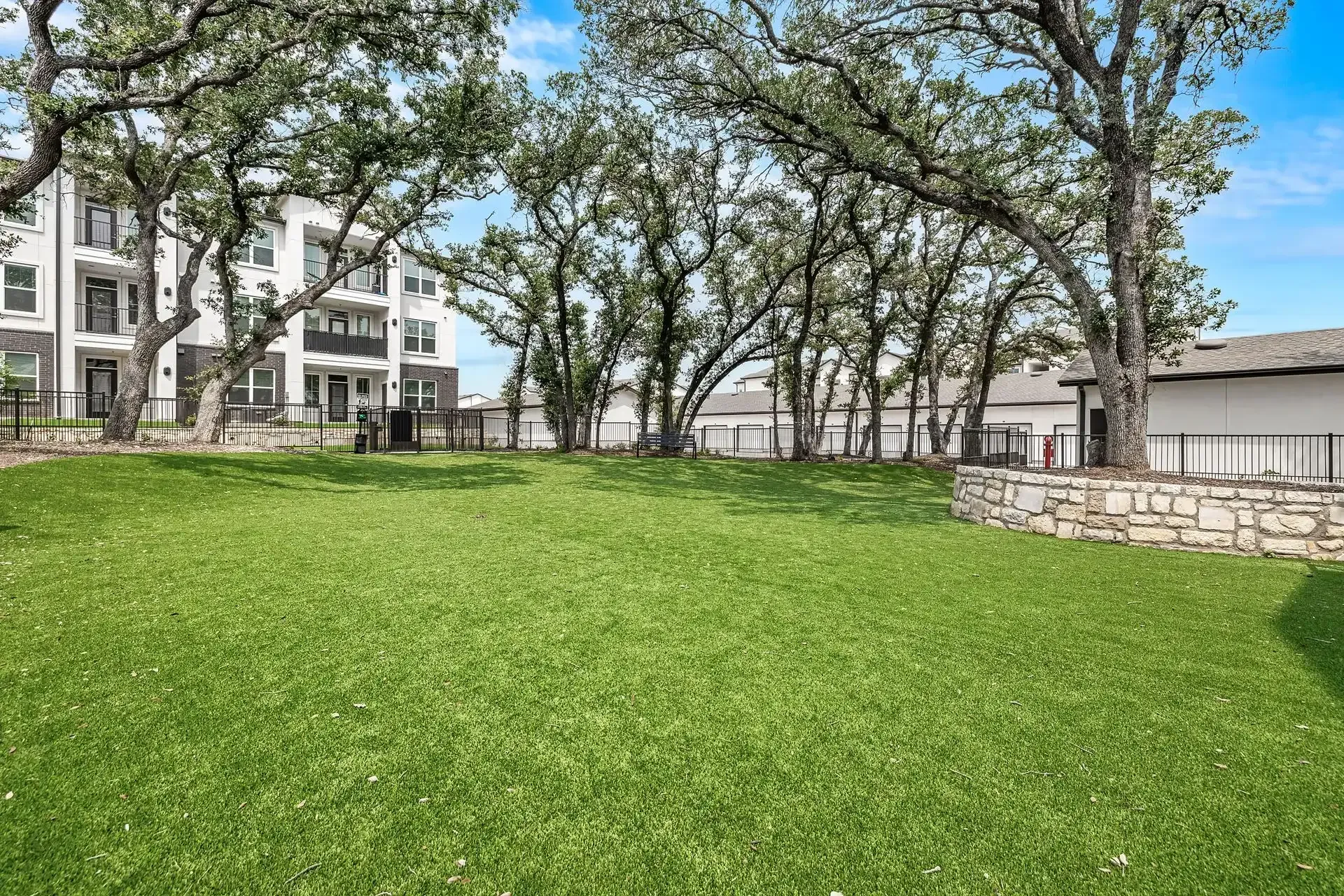 A large pet park with trees in the background and an apartment building at The Gabriel, which offers pet-friendly apartments for rent in Leander.