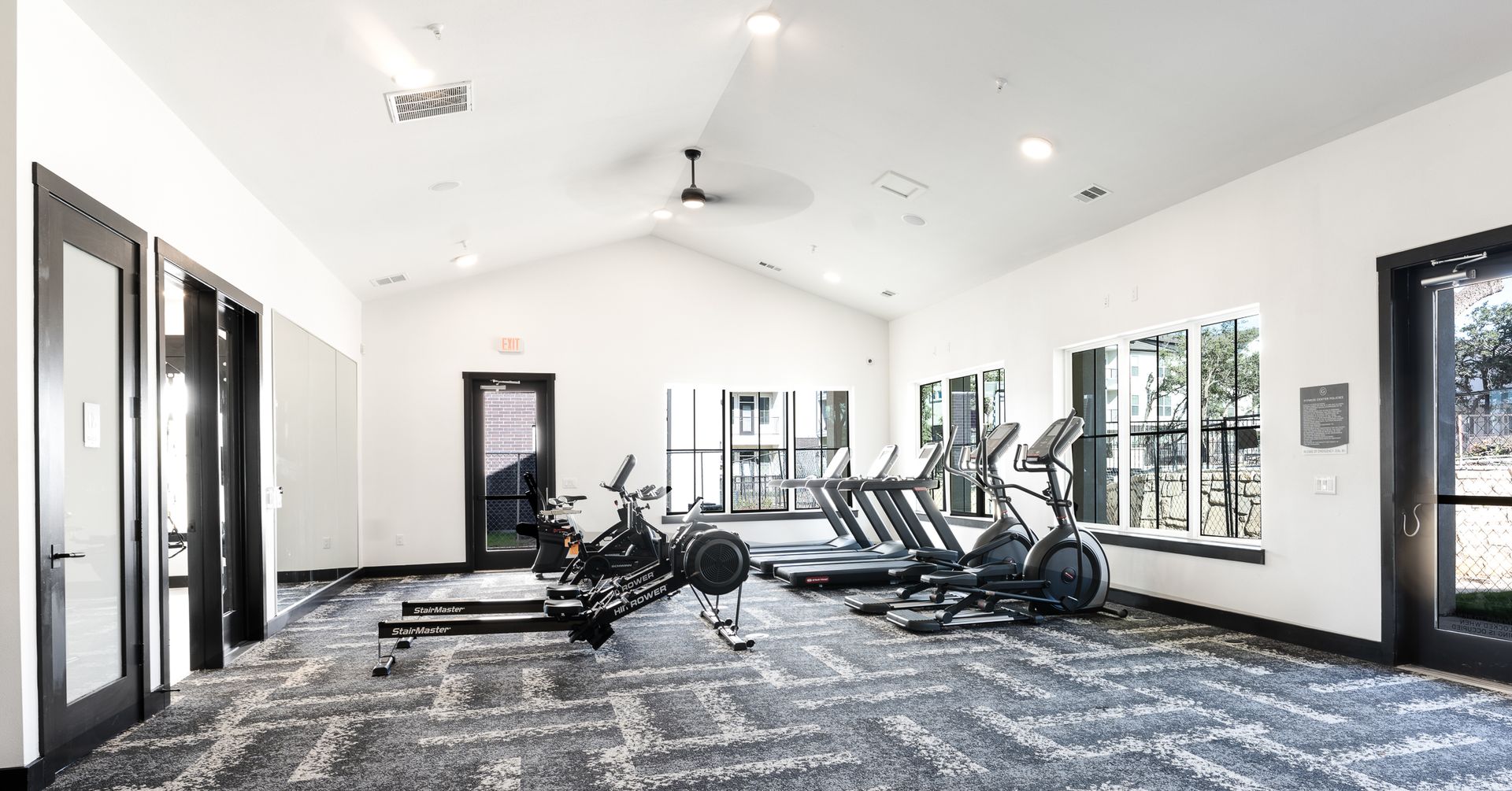 The Gabriel's apartment community gym, equipped with a variety of exercise machines and a ceiling fan, offers active apartment living in Cedar Park.