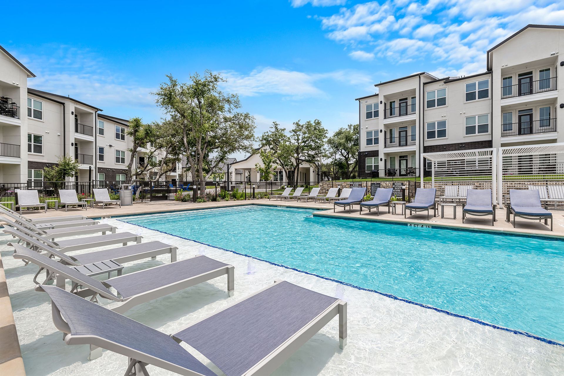 A large swimming pool surrounded by lounge chairs in front of an apartment building at The Gabriel, which offers apartments in Leander, TX.