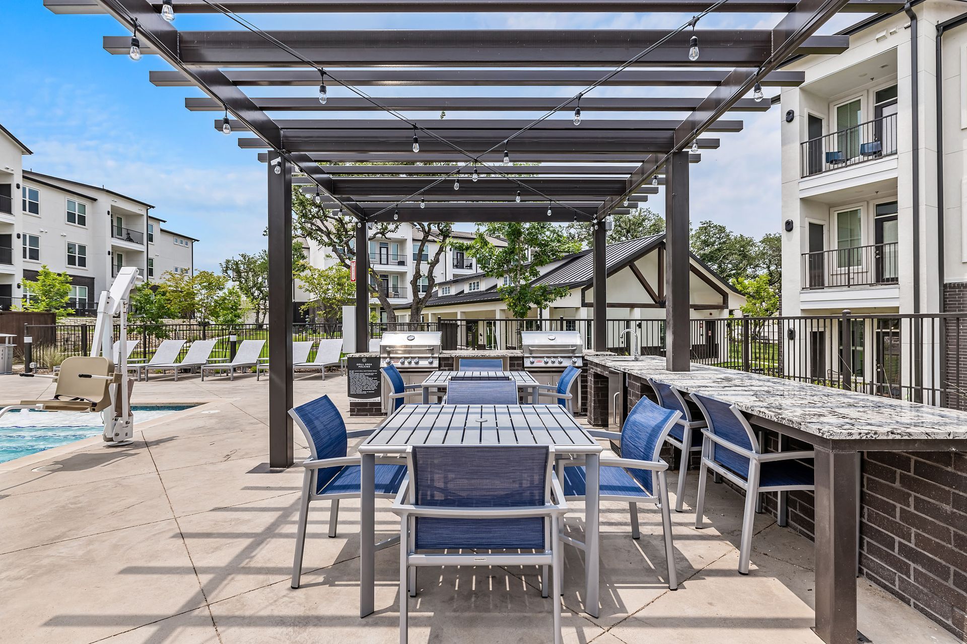 A table and chairs under a pergola next to a pool at The Gabriel, which offers pet-friendly Leander apartments near Charles Schwab.