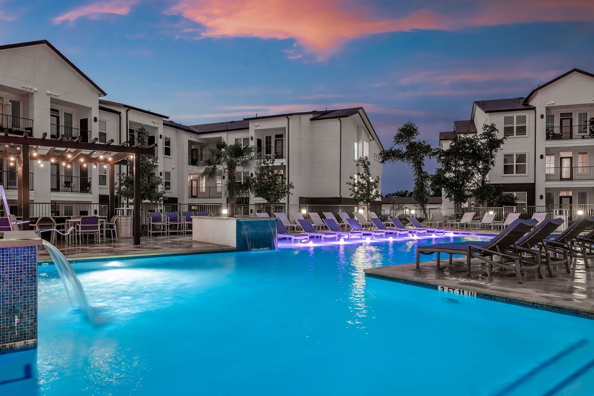 A large swimming pool with a waterfall in the middle, in front of the apartment building at The Gabriel, which offers open-concept apartments in Leander, TX.