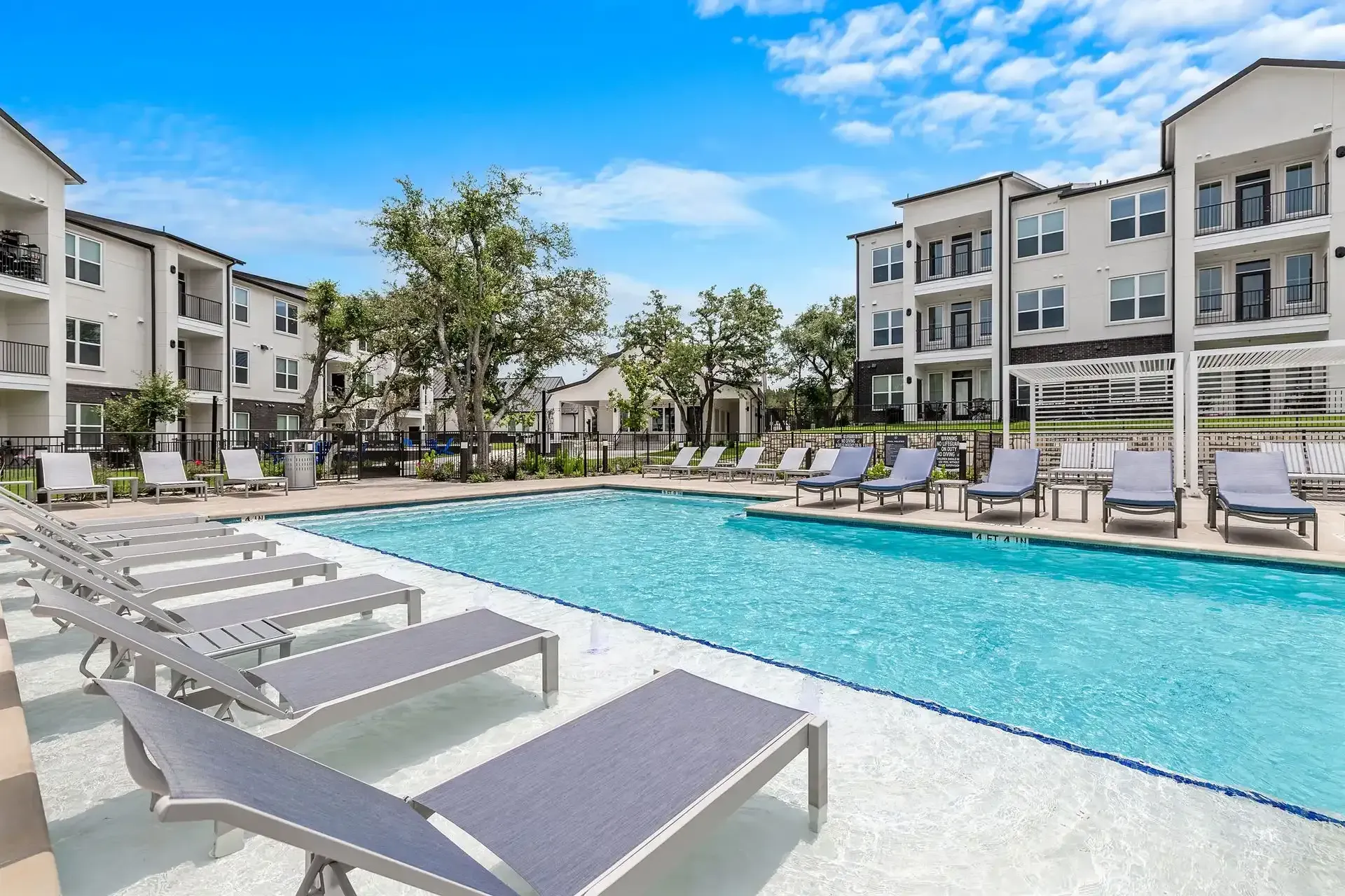 A large swimming pool surrounded by lounge chairs in front of an apartment building at The Gabriel, which offers apartments in Leander, TX.
