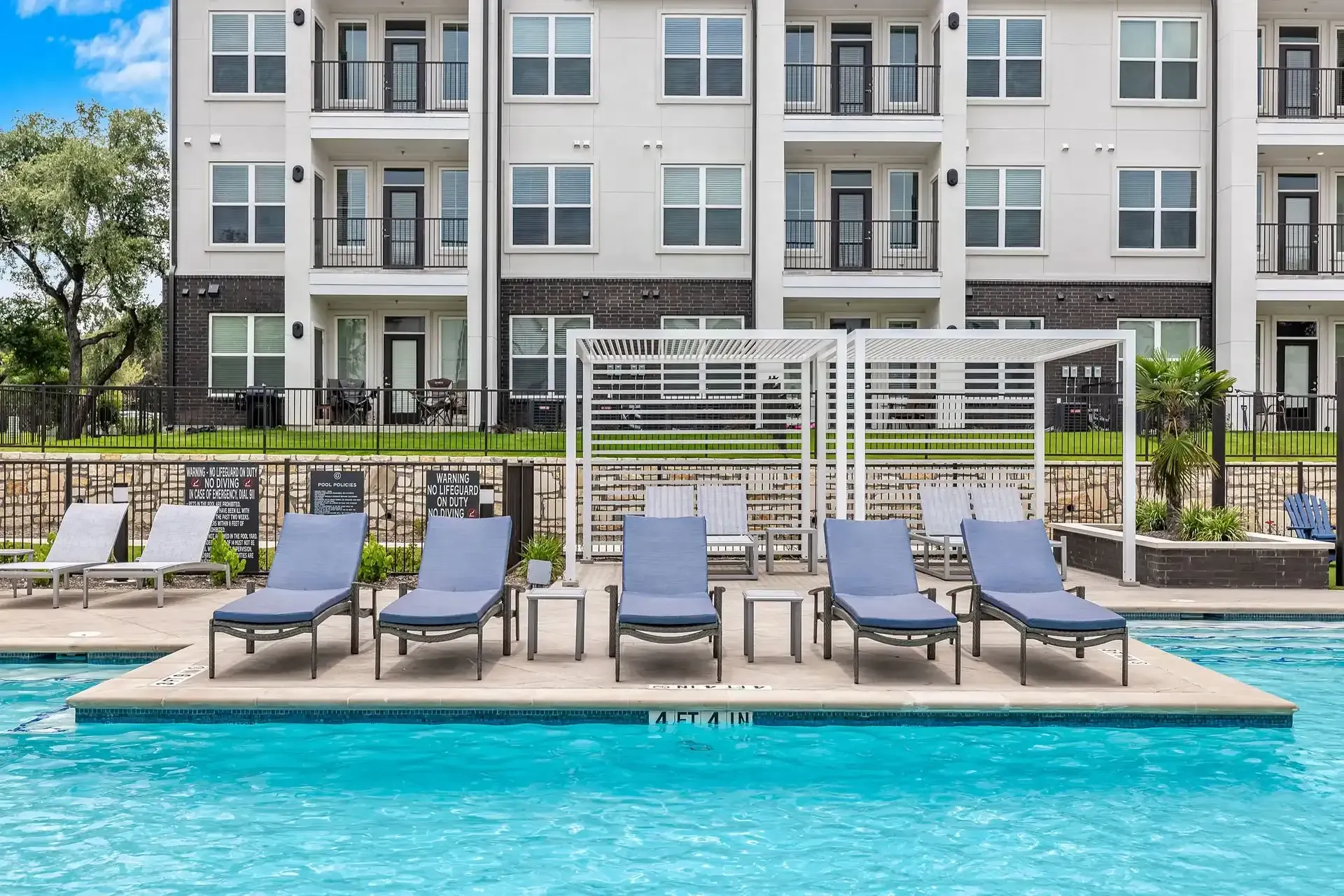 A large swimming pool surrounded by lounge chairs in front of an apartment building at The Gabriel, which offers apartments in Leander, TX.