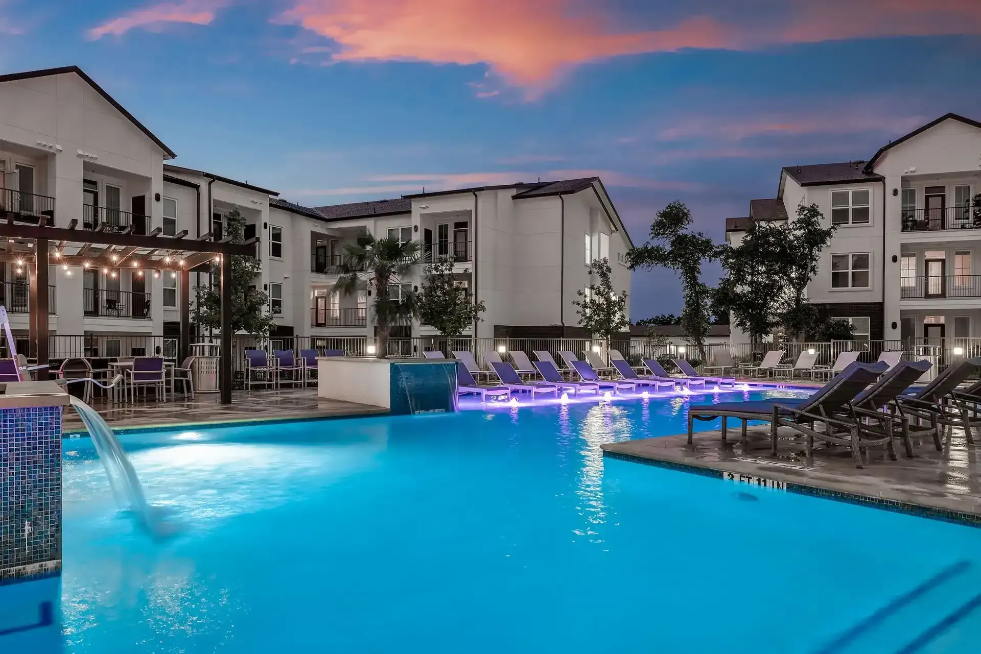 A large swimming pool with a waterfall in the middle, in front of the apartment building at The Gabriel, which offers open-concept apartments in Leander, TX.