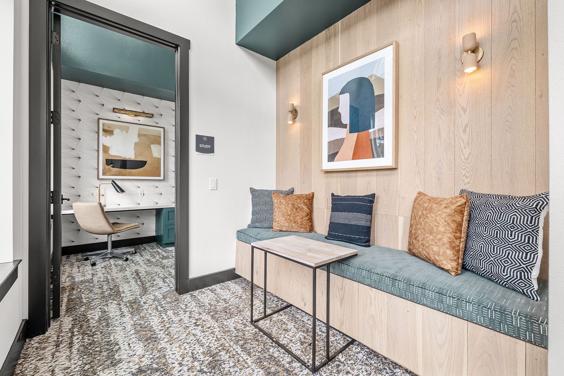 Apartment community work pod with a bench, table, chair, and painting on the wall at The Gabriel, which offers new apartments for rent in Leander, TX.