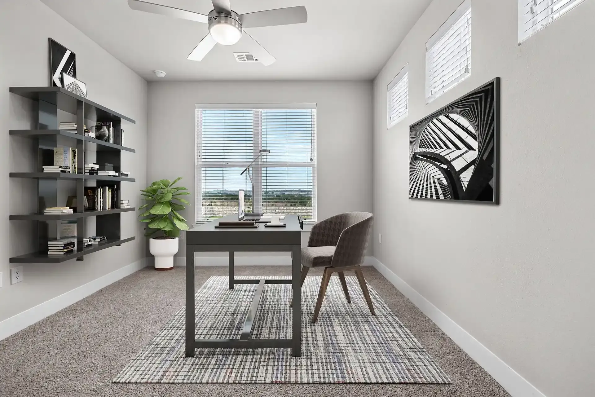 Home office with a desk, oversized window, wall art, plant, chairs, and a ceiling fan at The Gabriel, which offers pet-friendly apartments near Georgetown, TX.