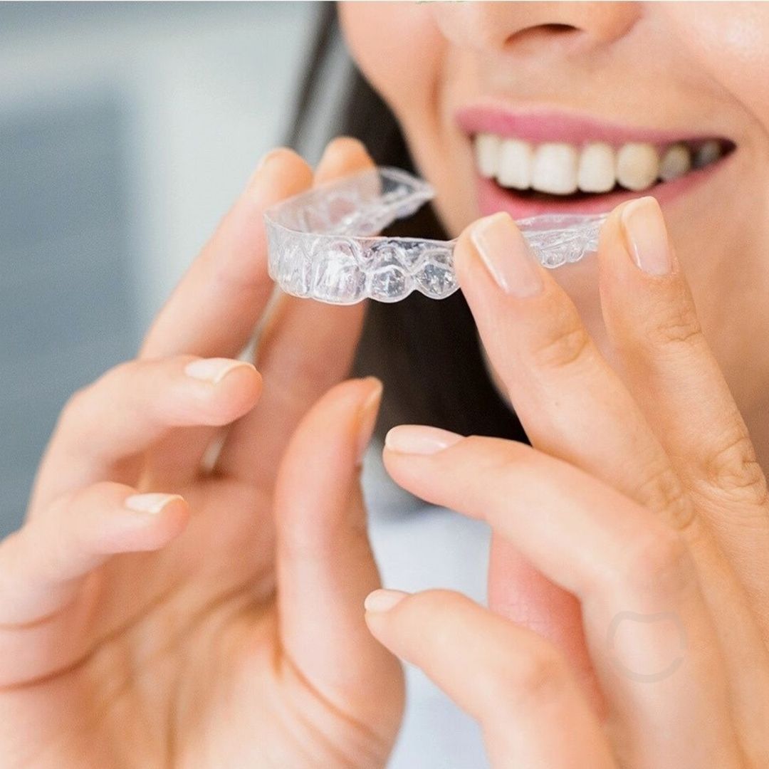 Woman holding clear orthodontic aligners near her mouth, smiling.