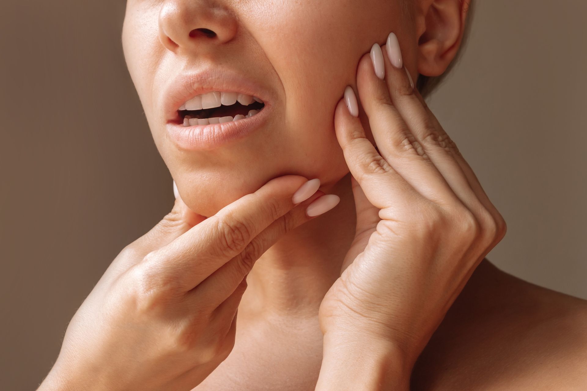 Woman with mouth open, face scrunched in pain, hands touching her jaw and cheek, presumably experiencing toothache.