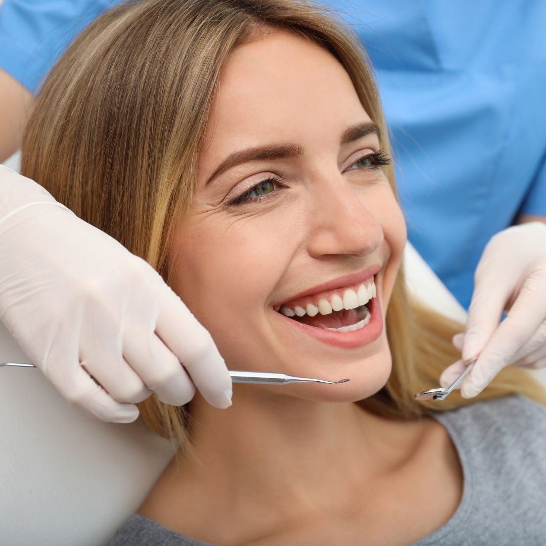 Woman smiling during a dental exam, dentist holding instruments, in a dental office.