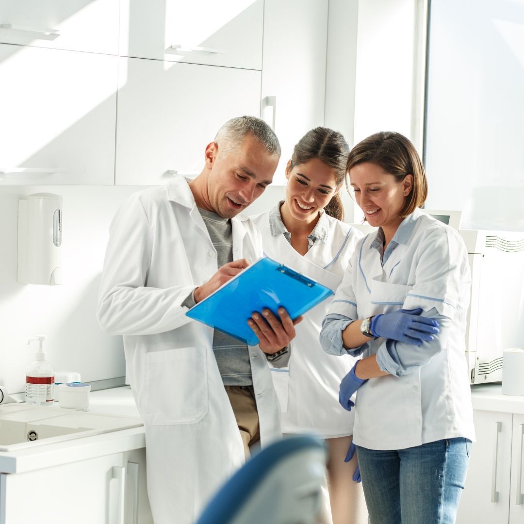A dentist and two dental assistants reviewing a chart in a bright dental office, all smiling.
