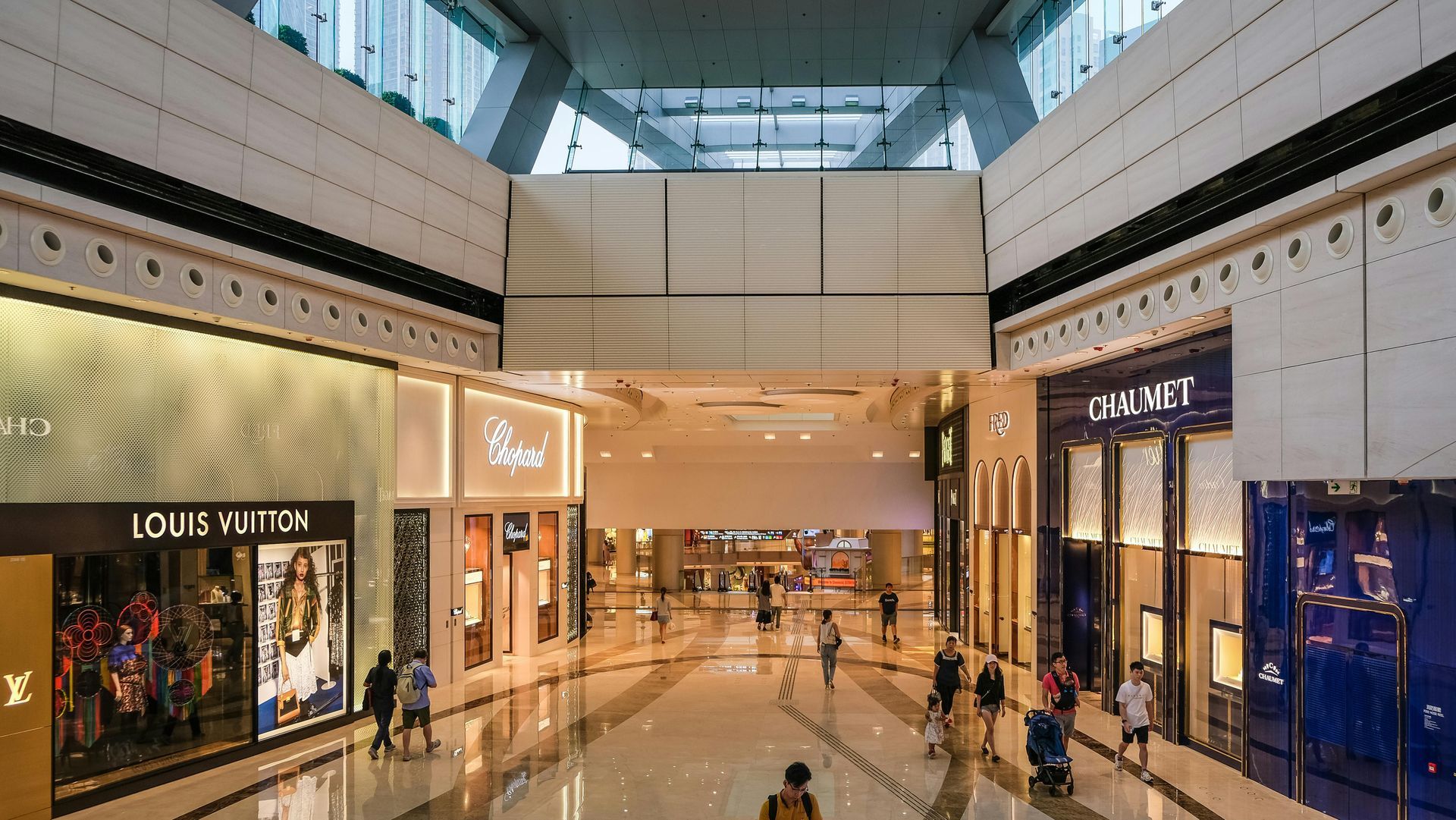 A luxury mall interior with high-end brand stores, people walking.