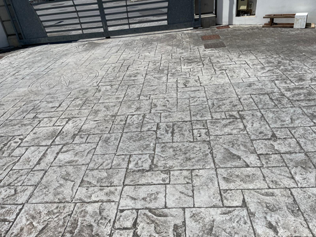 Cortile pavimentato con motivi in ​​pietra, adiacente a un cancello metallico e al muro di cinta dell'edificio.
