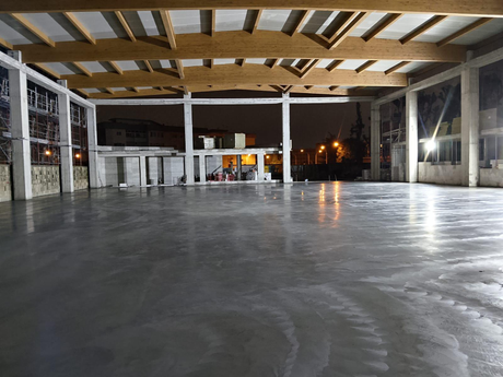 Padiglione interno vuoto con pavimento in cemento lucidato e travi in ​​legno a vista, di notte.