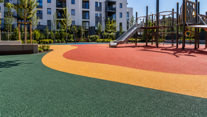 Parco giochi colorato con scivolo e struttura per arrampicata accanto a moderni palazzi residenziali.