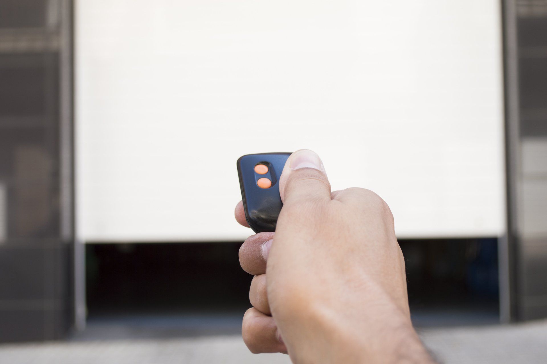 A person is holding a remote control in front of a garage door.