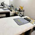 Massage room with two treatment tables, gray towels, and small black carts against white walls.