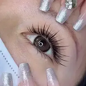 Close-up of a brown eye with long lashes and silver glitter nails framing it