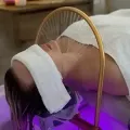 Person lying on a spa treatment bed with a white headband and a purple-lit facial device over the face
