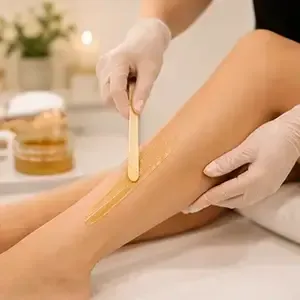 Gloved hands applying wax to a leg with a wooden spatula in a spa setting