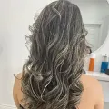 Long wavy dark hair with silver highlights viewed from behind in a bright room, shown in a mirror.