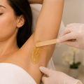 Gloved technician applying wax to an underarm with a wooden spatula in a spa setting