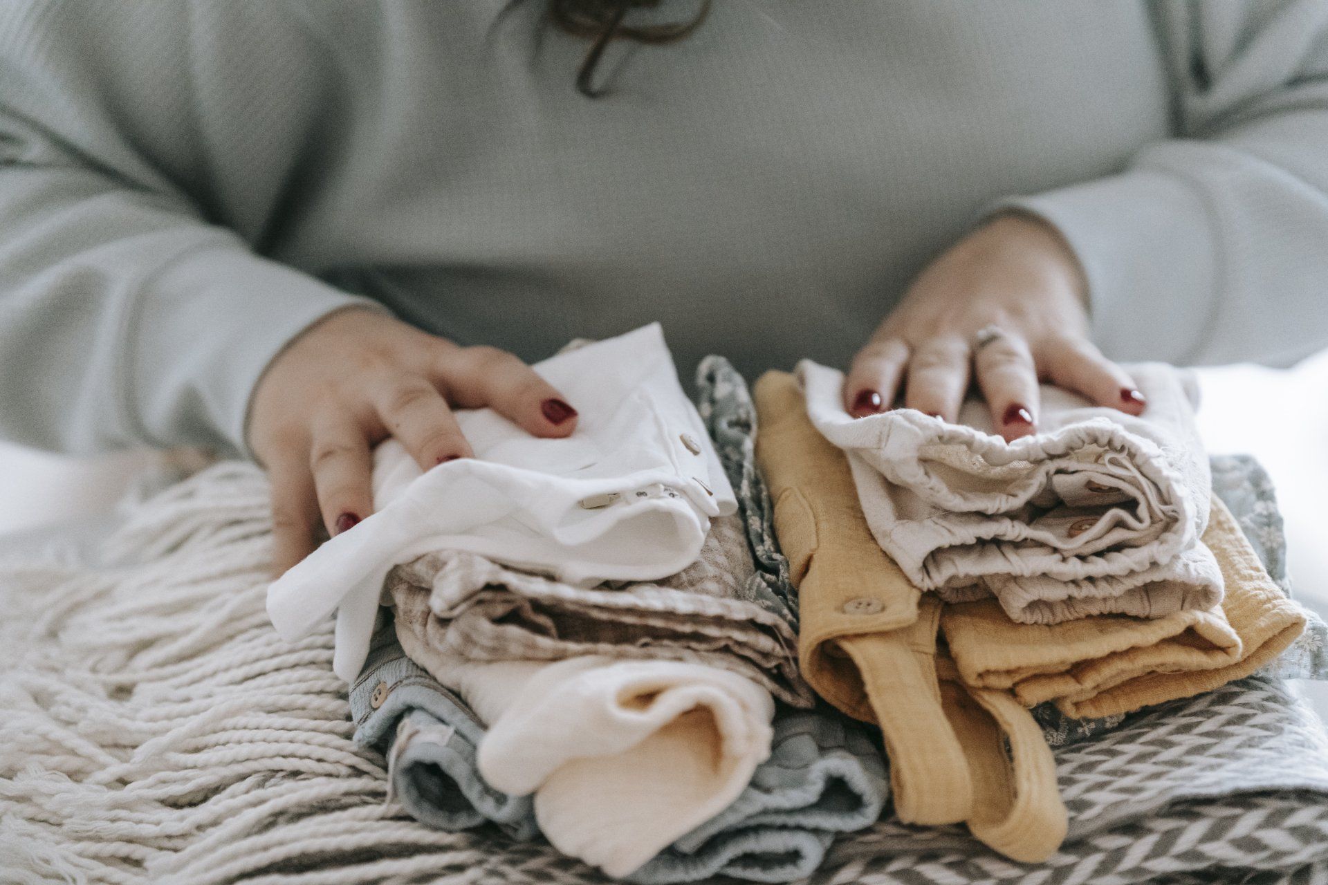 A woman is holding a pile of clothes on a blanket.