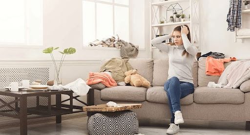 Stressed woman on messy couch surrounded by clutter before spring decluttering.