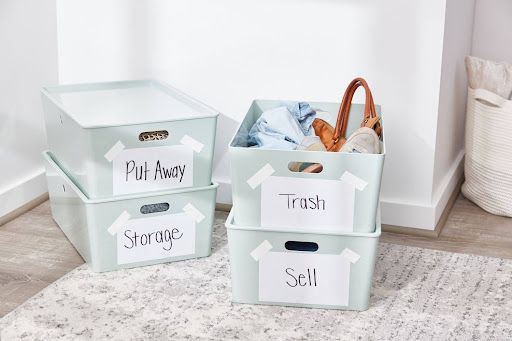 Bins labeled Put Away, Storage, Trash, and Sell with clothes and accessories for spring decluttering checklist.