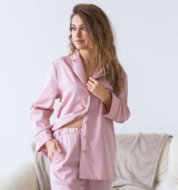 A woman in a pink pajama set is standing next to a couch.