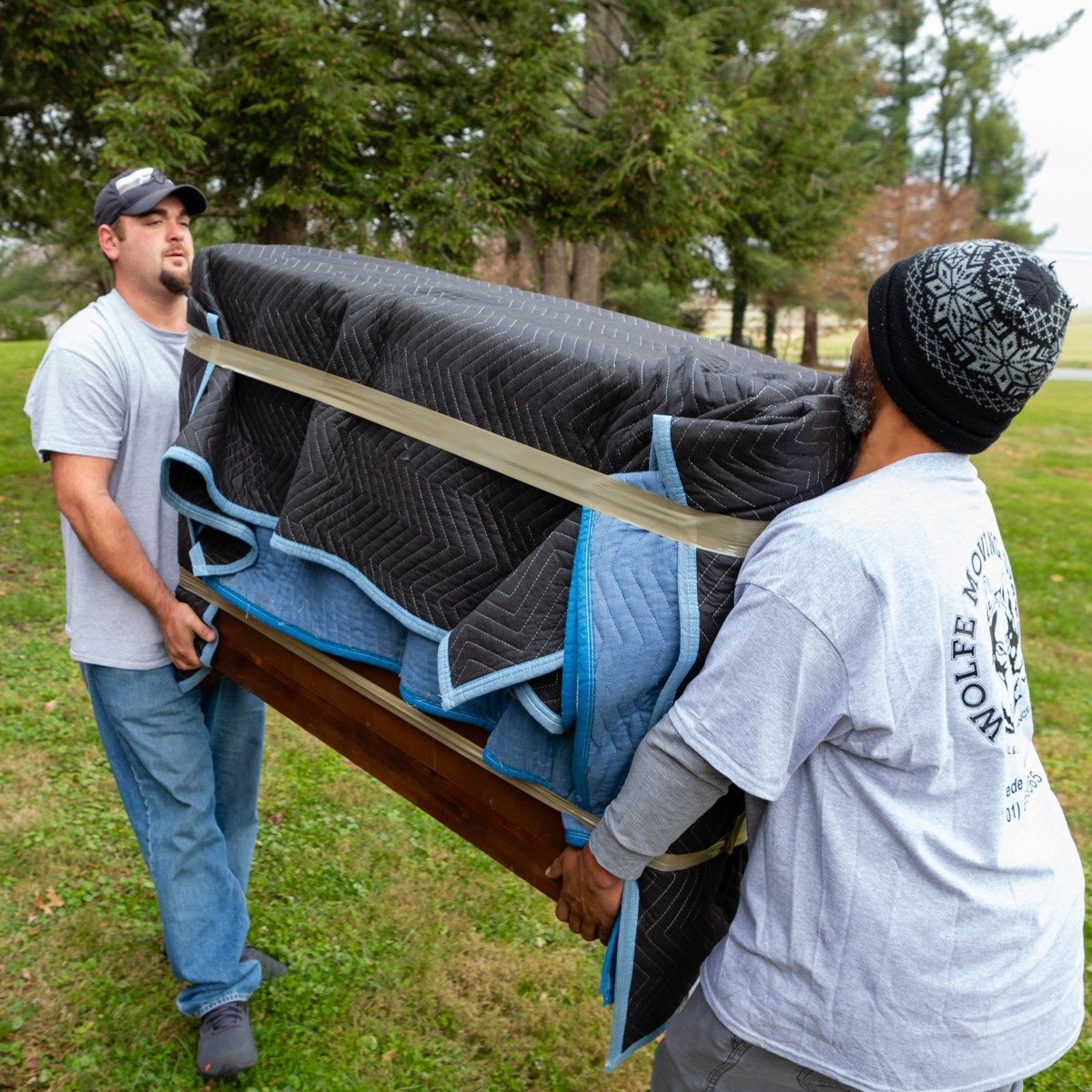 A man wearing a wolfe shirt is carrying a piano.