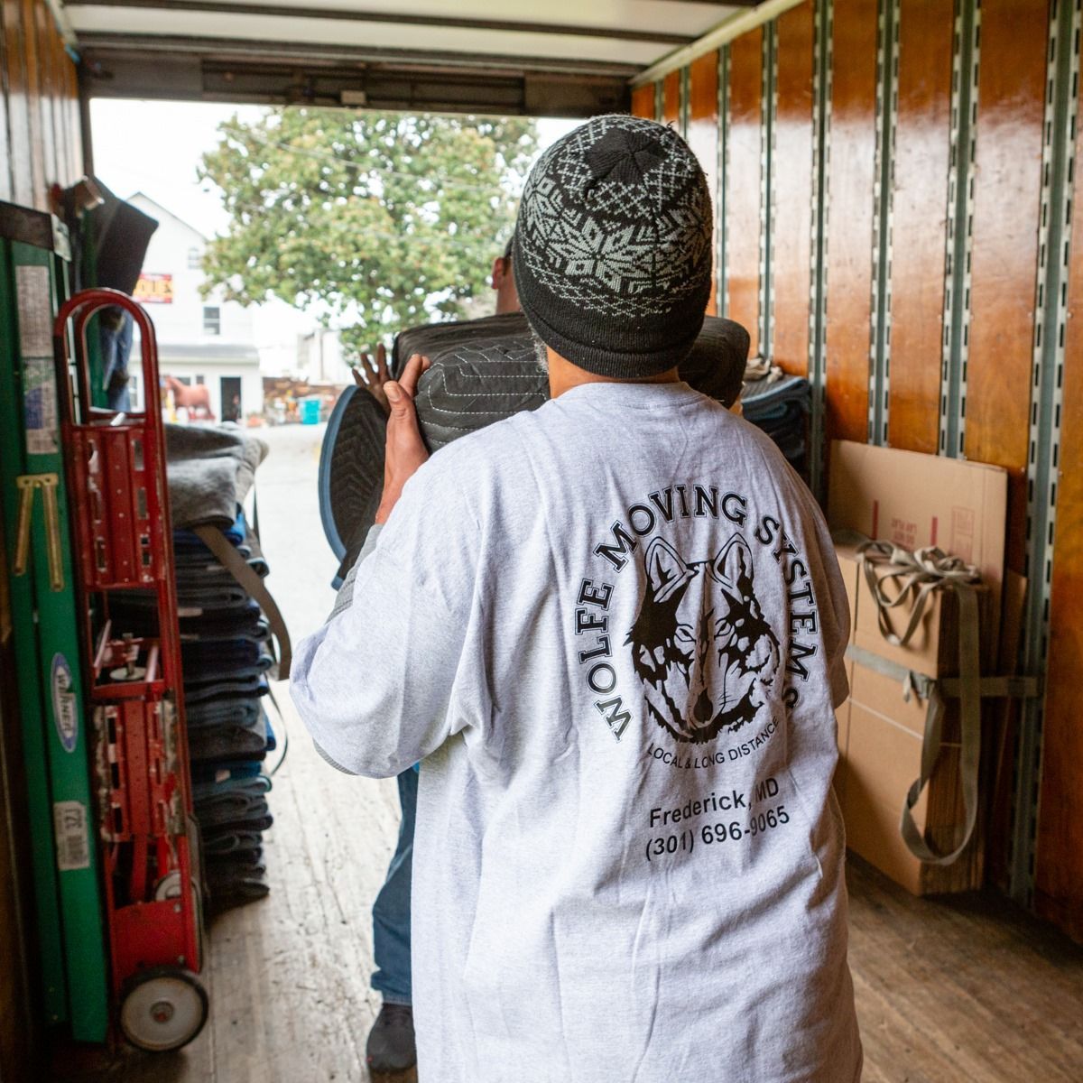 A man wearing a wolfe moving system shirt is carrying a chair.