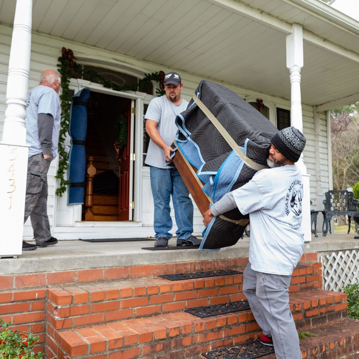 A man is carrying a large piece of furniture on a porch.