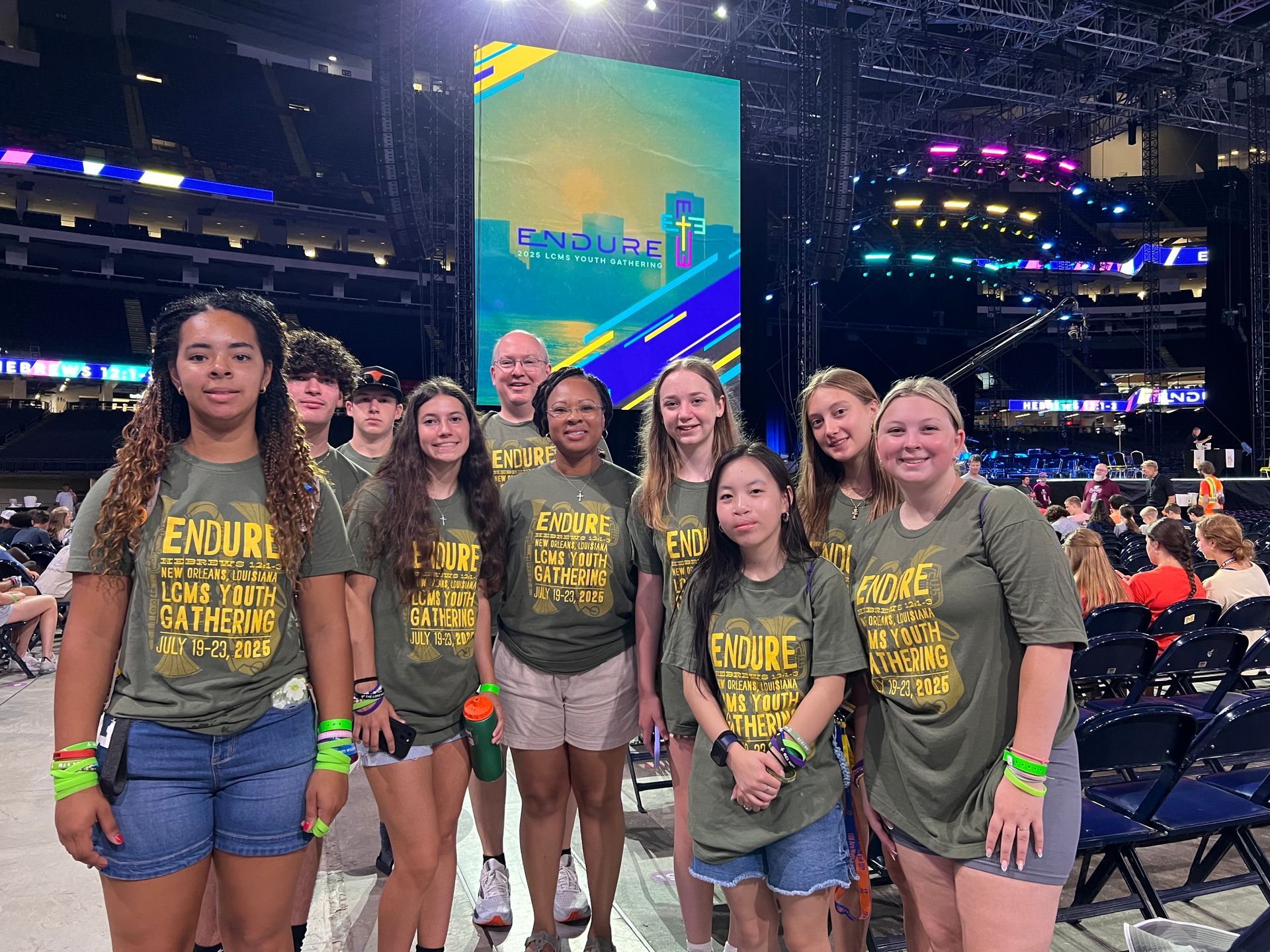 Group of people in green shirts at an event. Large screen with cityscape backdrop.