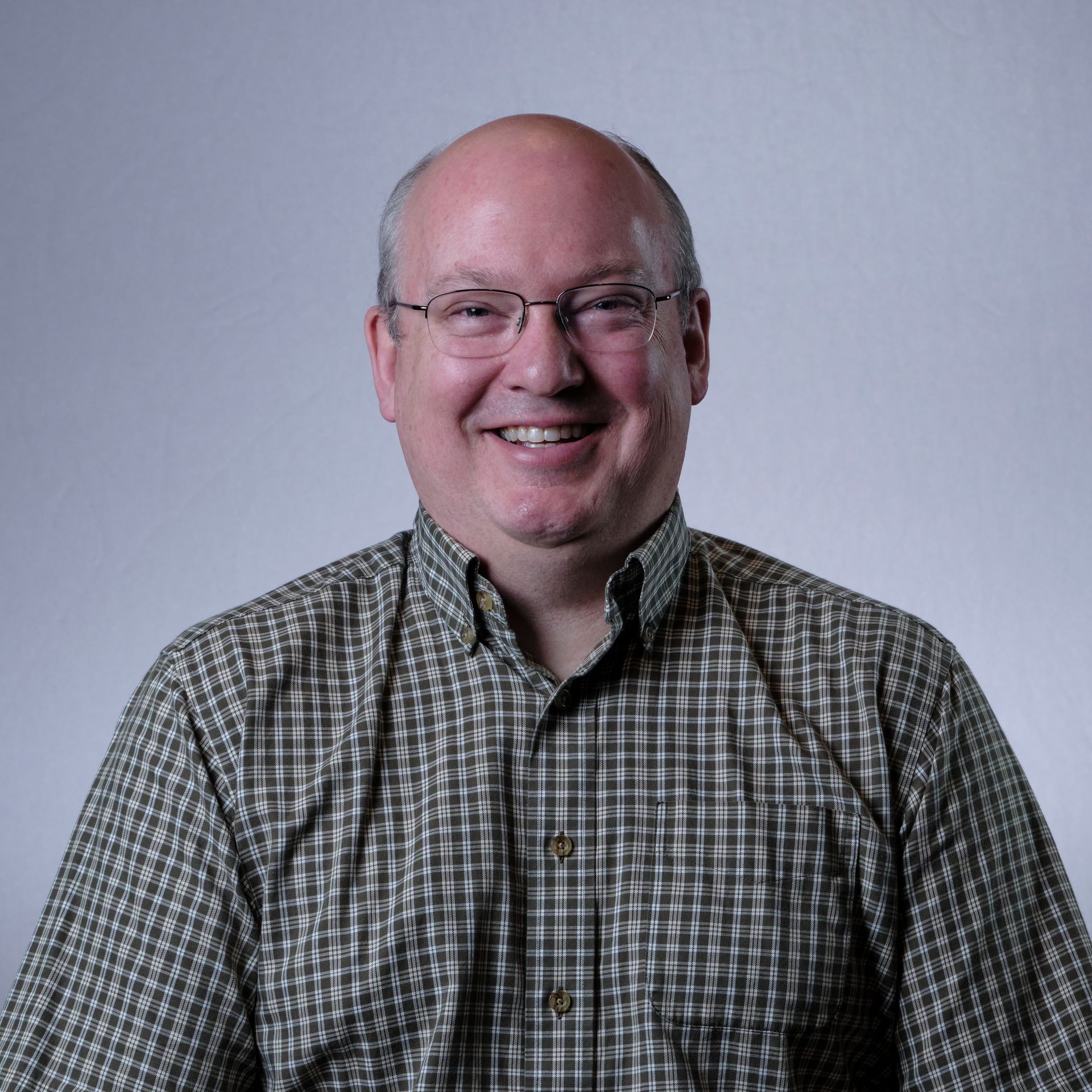 Bald man in glasses smiles, wearing a checkered shirt.