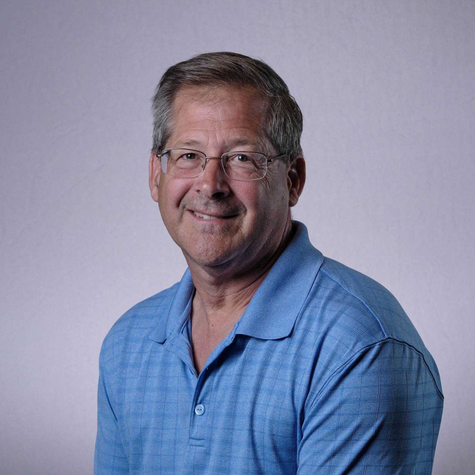 Man with glasses and a blue shirt smiles, looking towards the camera.