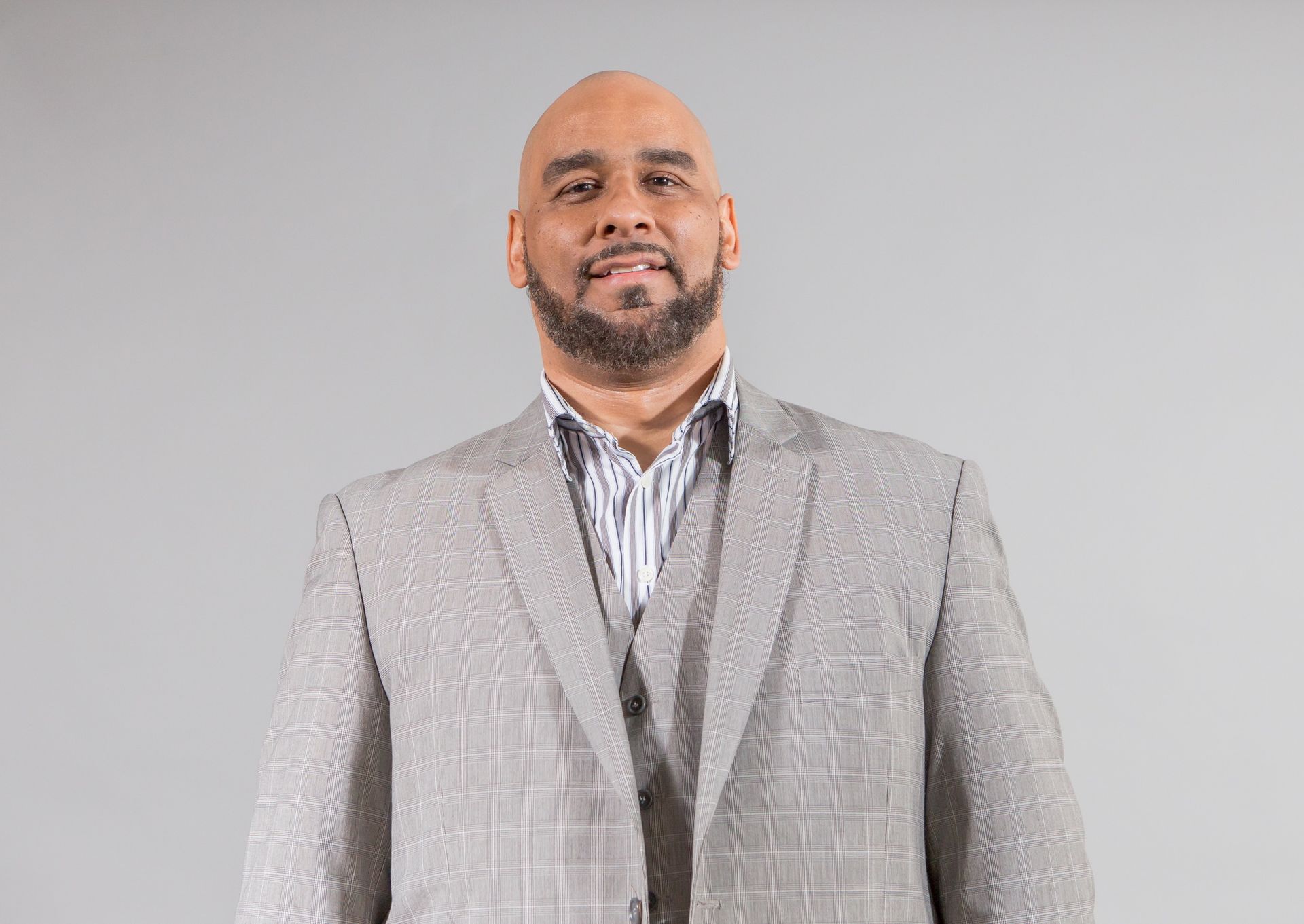 Man in a grey plaid suit smiling, set against a grey background.