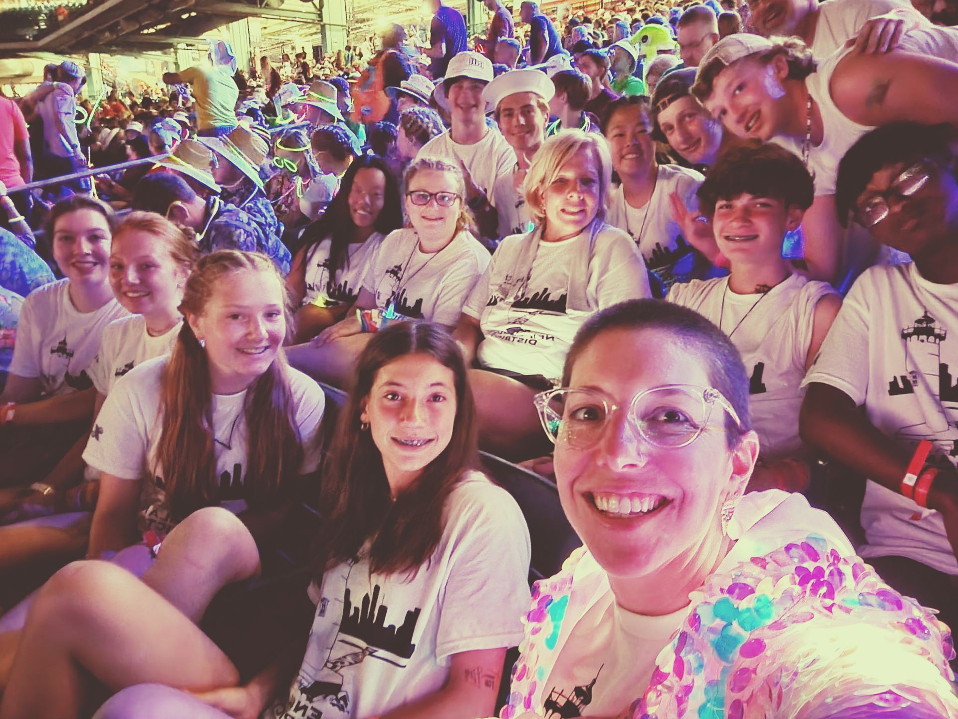 Group of people smiling at the camera, mostly in white shirts, likely at an outdoor event.