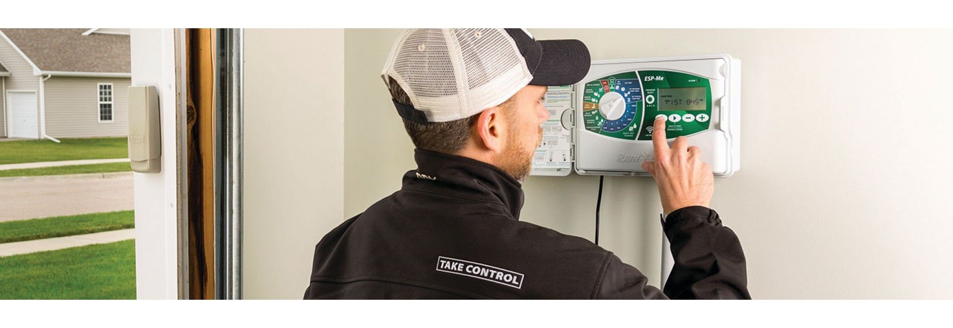 A person adjusting a control panel on a wall, house in the background.