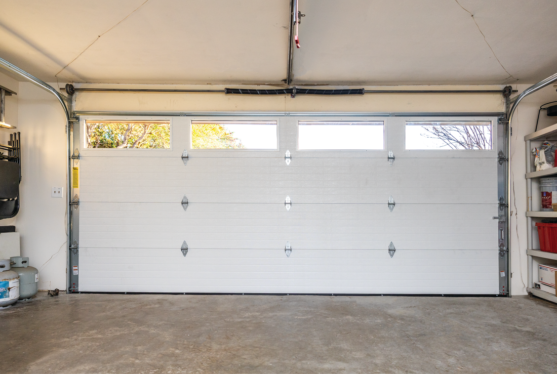 An empty garage with a white garage door and shelves.