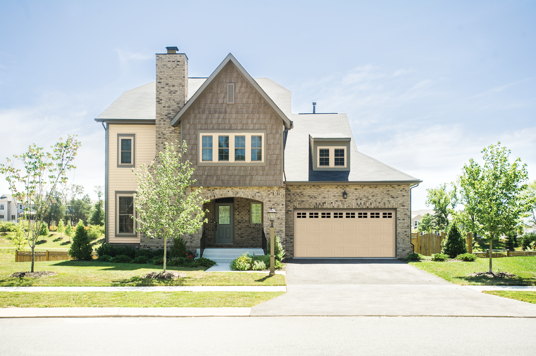 A large house with a tan garage door is sitting on top of a lush green lawn.