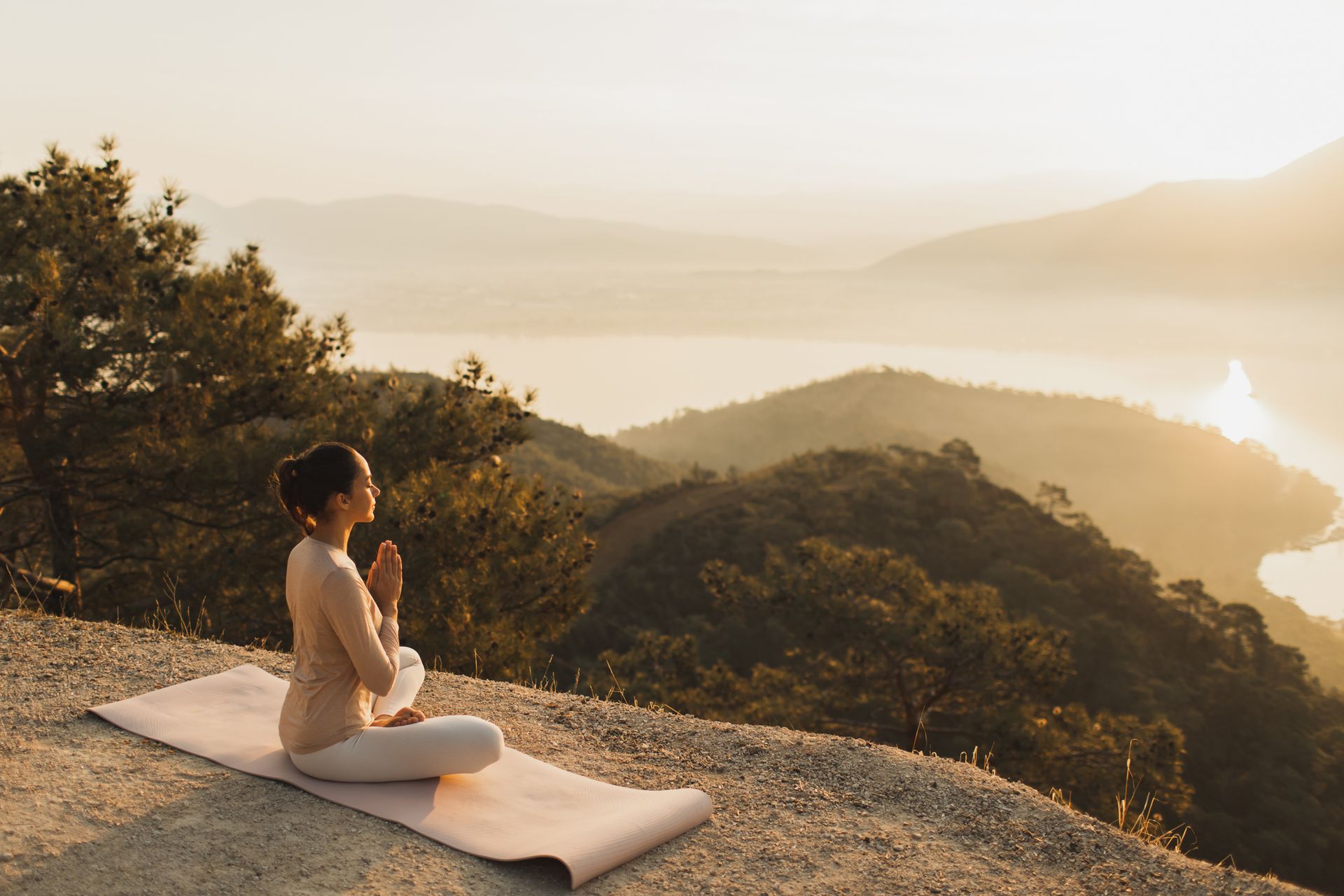 A woman is sitting on a yoga mat on top of a mountain.