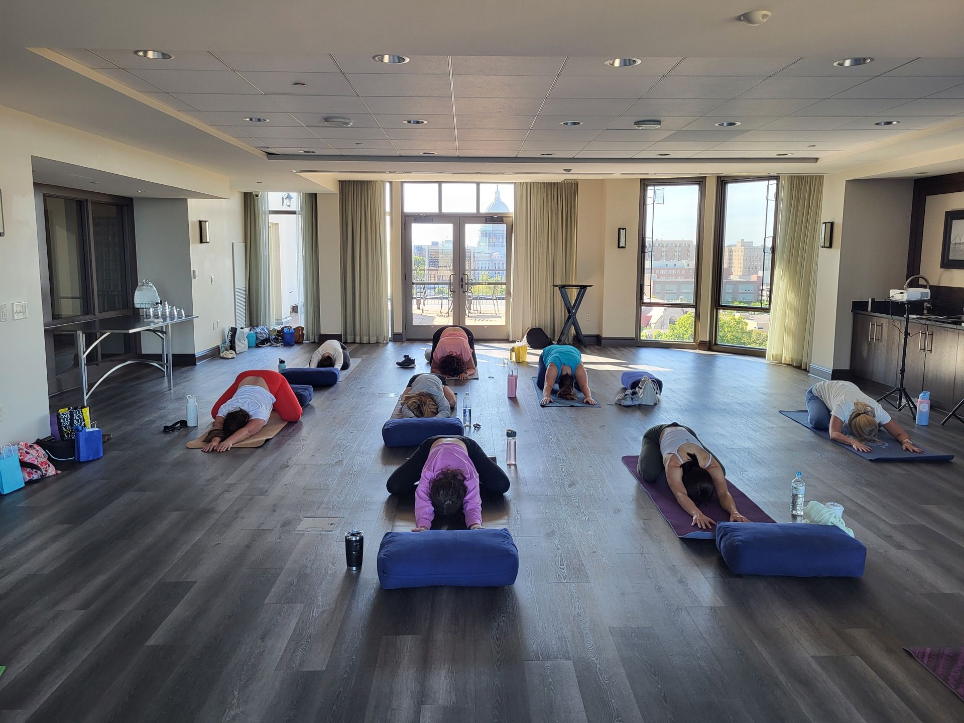 A woman is helping another woman do a yoga pose on a mat in a gym.