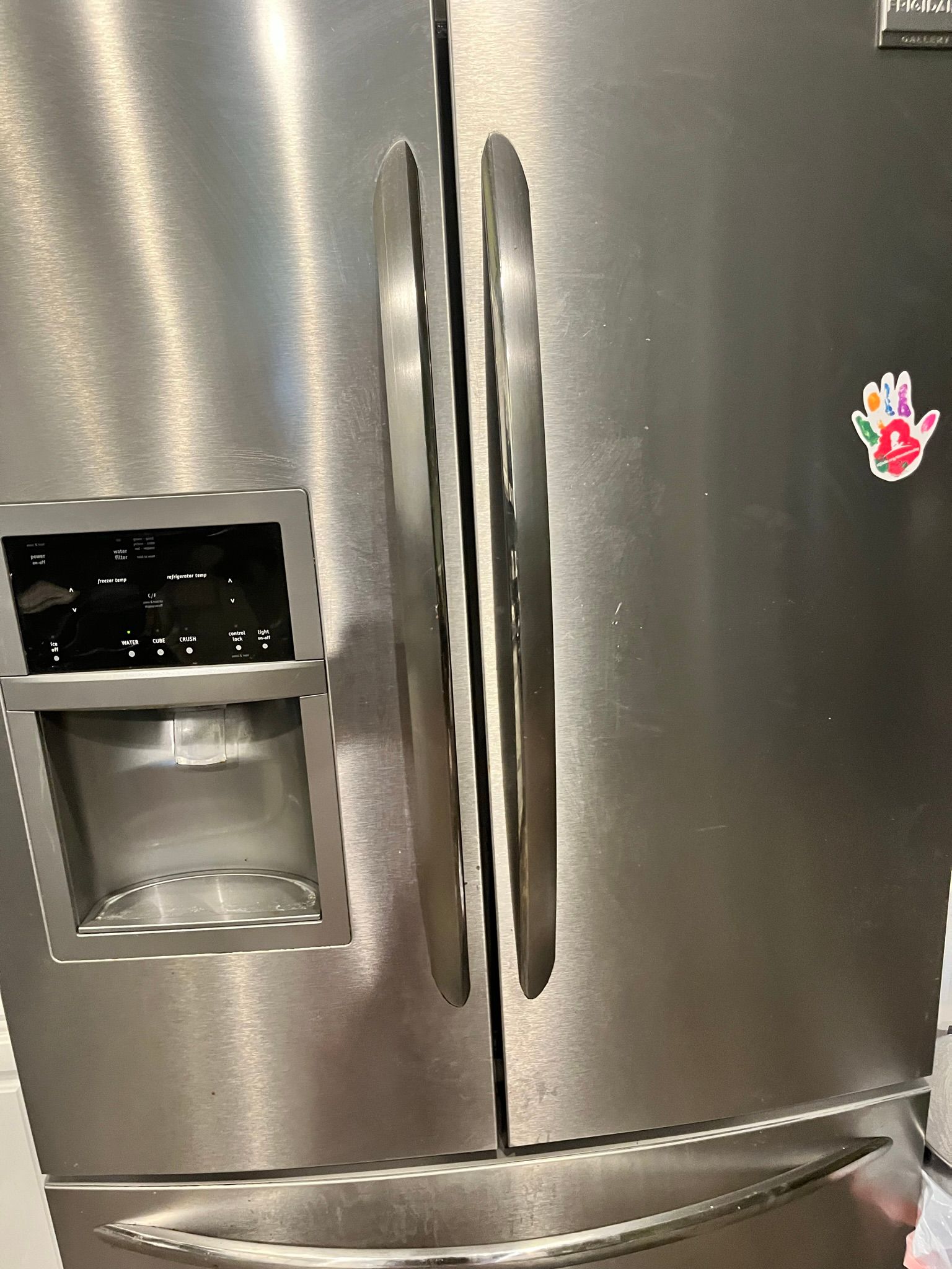 Stainless steel refrigerator with a water dispenser and a small handprint sticker.