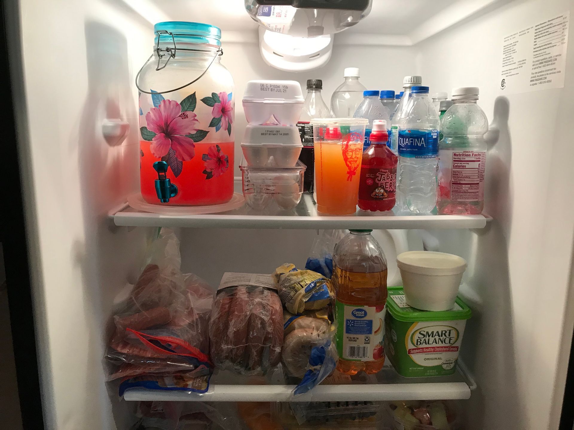 Refrigerator interior: Drinks and containers of food on shelves, including a large decorated jar.