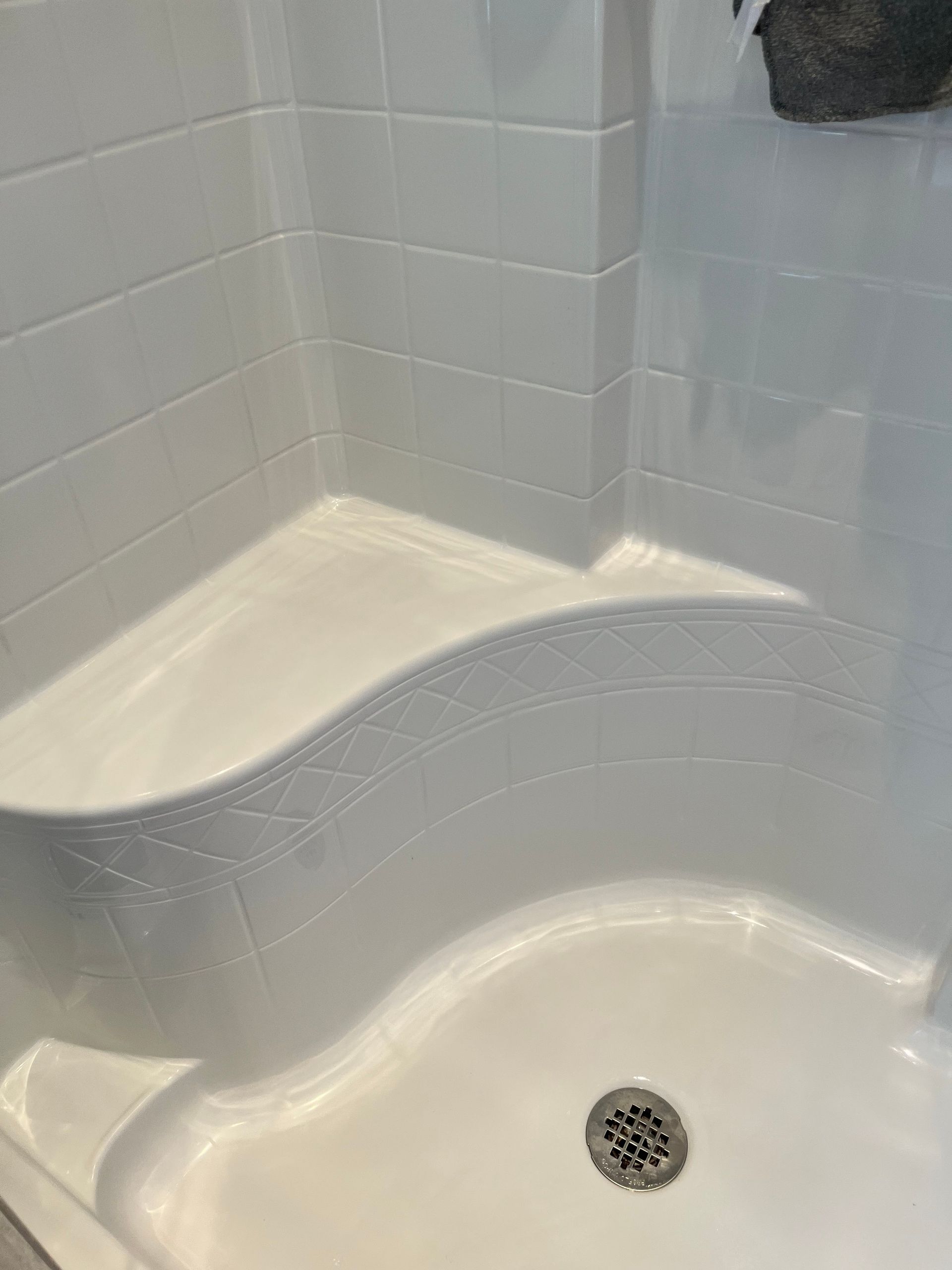 White, molded, accessible shower stall with built-in seat. A drain is visible on the shower floor.