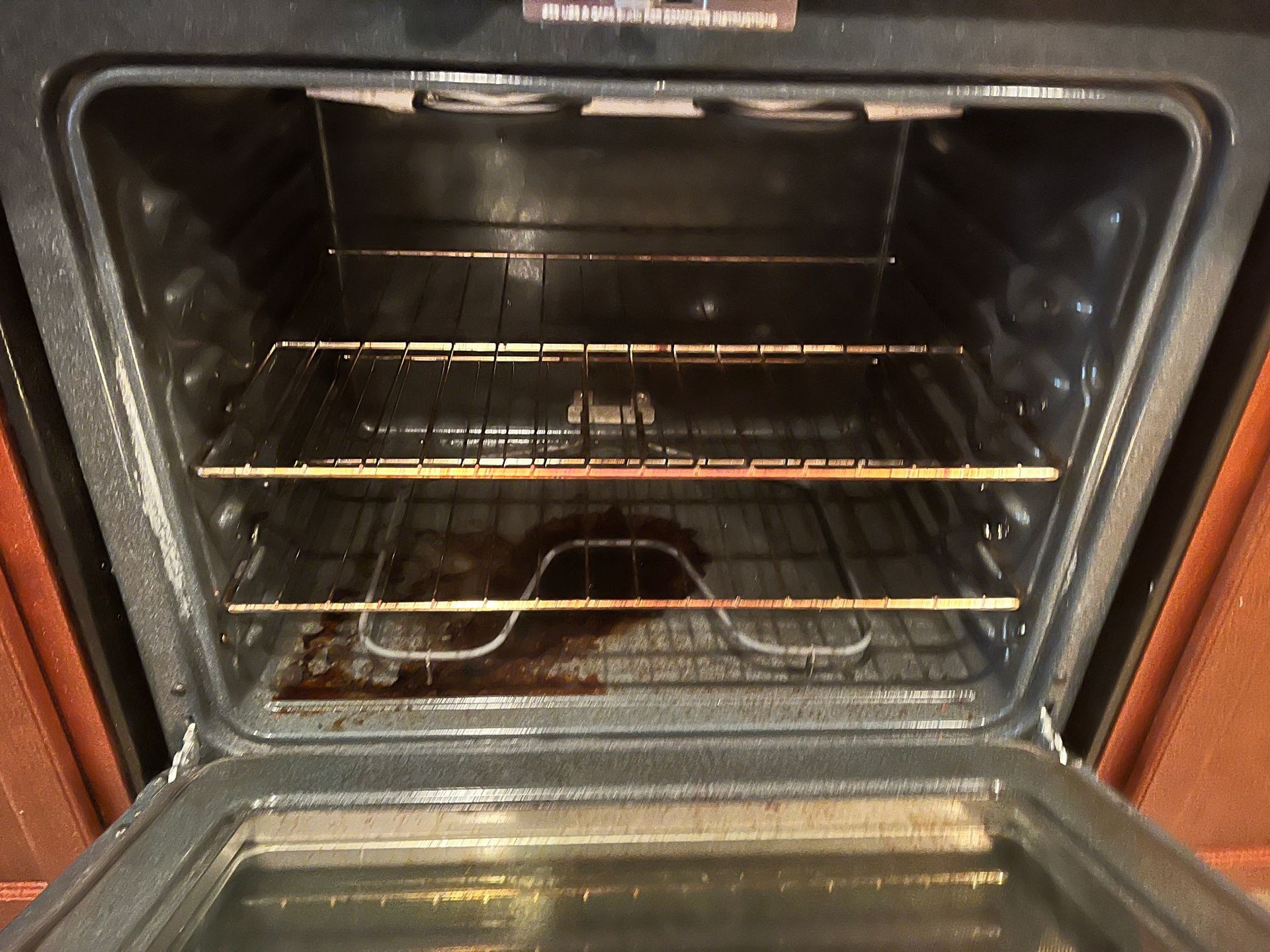 An open oven interior with three racks. Brown stains are visible on the bottom and a heating element.