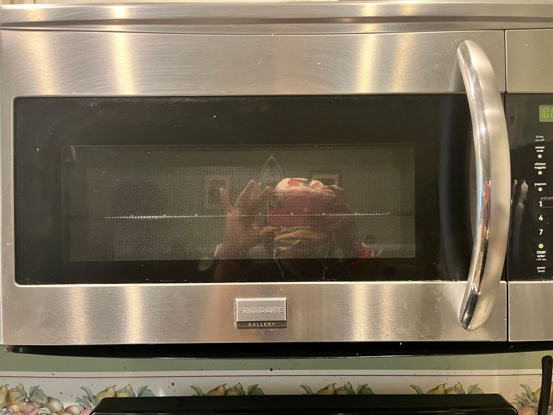 A stainless steel microwave with food inside, possibly cooking. Front view.
